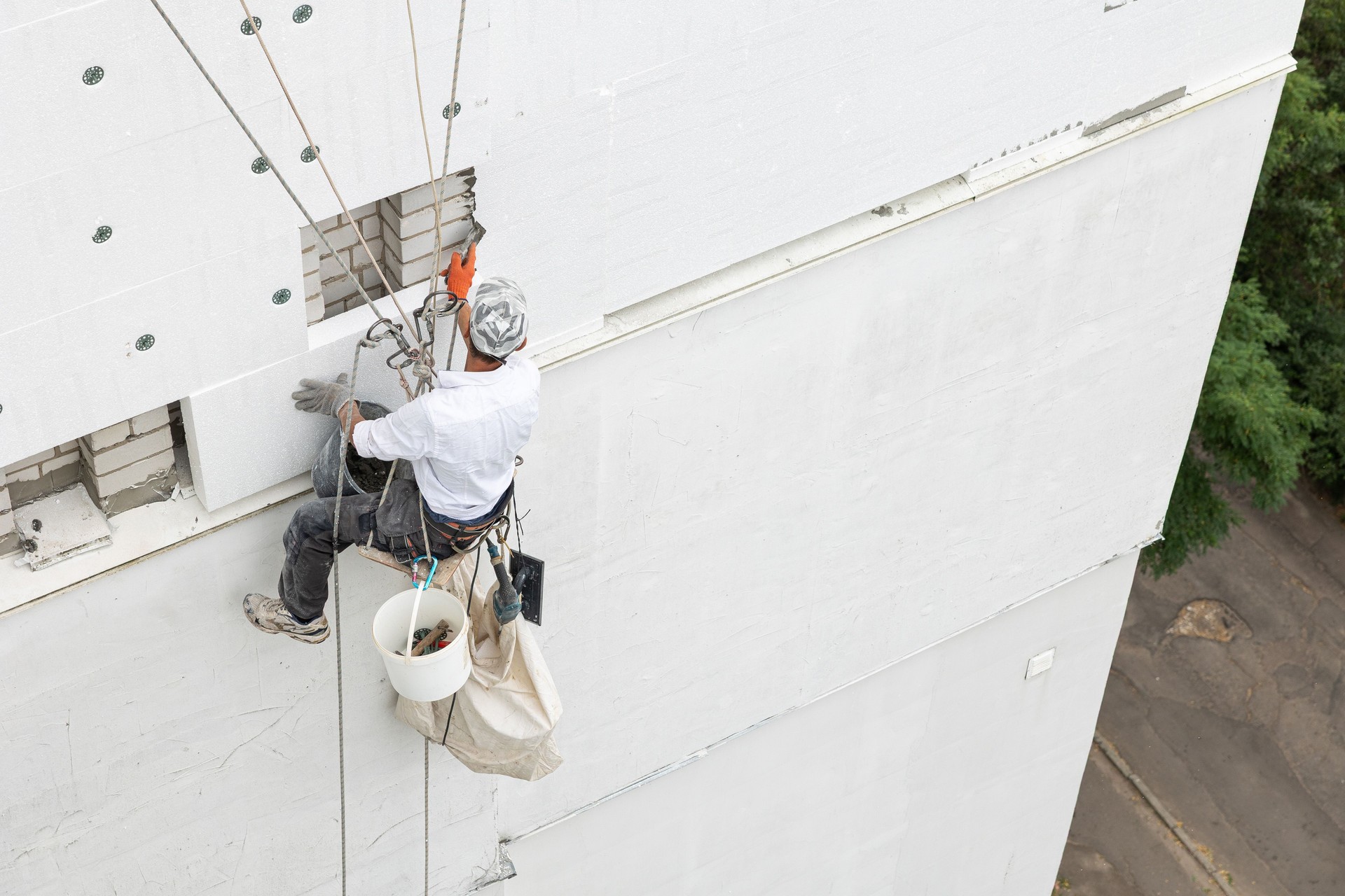 Construction worker insulating the exterior wall of a building with polystyrene panels at height.