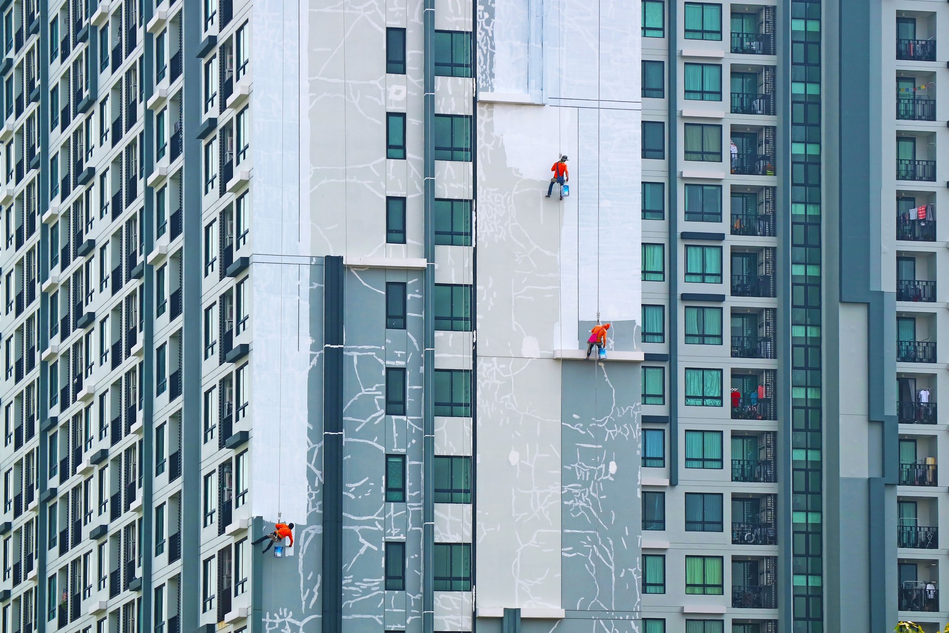 Three of rope access workers painting the facade of a high residential buildings